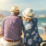 Couple of seniors seated by the sea on vacation, watching a phone, relaxed and summer atmosphere