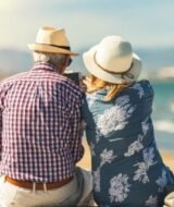 Couple of seniors seated by the sea on vacation, watching a phone, relaxed and summer atmosphere