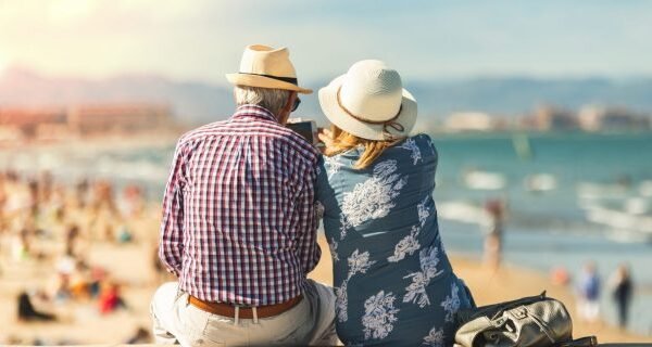 Couple of seniors seated by the sea on vacation, watching a phone, relaxed and summer atmosphere
