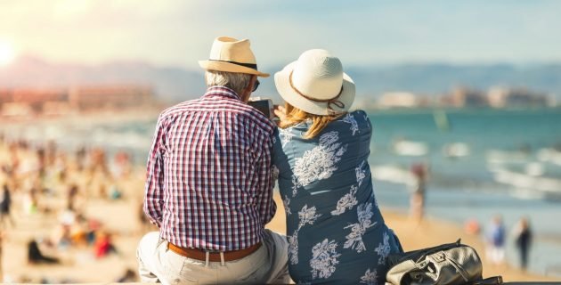 Couple of seniors seated by the sea on vacation, watching a phone, relaxed and summer atmosphere